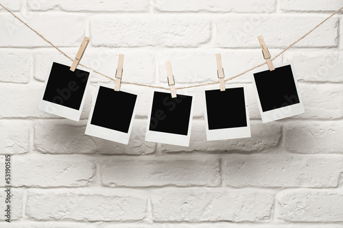 Fototapeta na wymiar Blank photos hanging on a clothesline over brick wall background