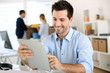 © goodluz - Smiling man in office working on digital tablet