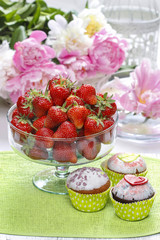 Wall Mural - Glass bowl of strawberries and green cupcakes on green napkin.