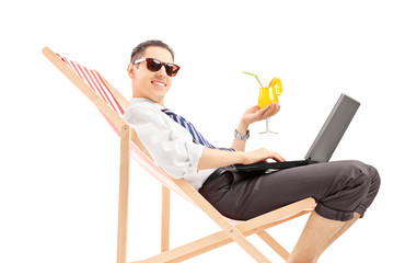 Canvas Print - Smiling busy man with laptop sitting on a beach chair and holdin