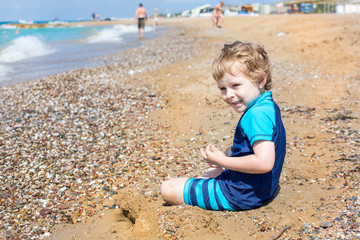 Wall Mural - Little toddler boy playing with sand and stones on the beach