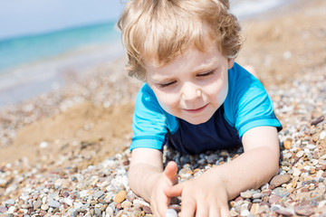 Wall Mural - Little toddler boy playing with sand and stones on the beach