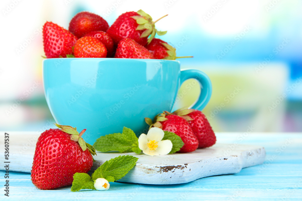 Ripe sweet strawberries in cup on blue wooden table