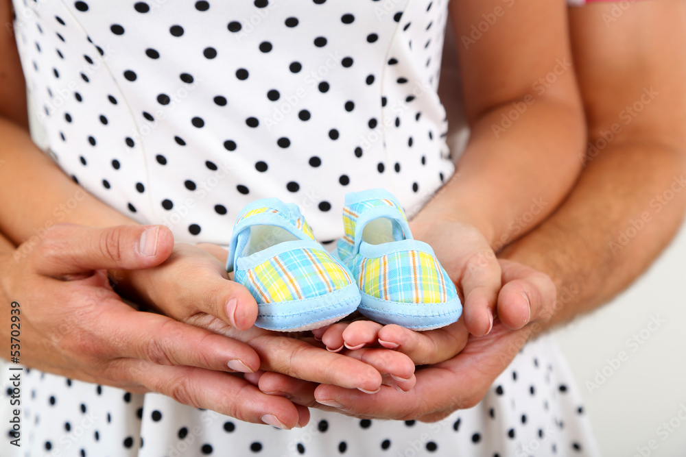 Young married couple with baby clothes on grey background