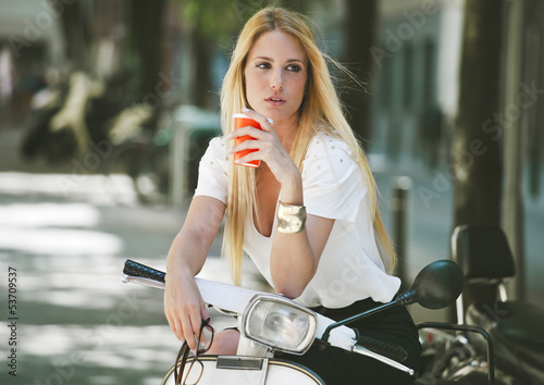 Naklejka dekoracyjna Young businesswoman drinking a coffee on a italian scooter.