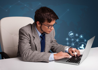 Young man sitting at desk and typing on laptop with social netwo