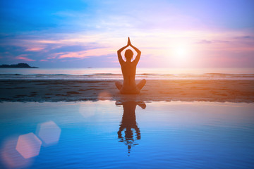 Wall Mural - Silhouette young woman practicing yoga on the beach at sunset