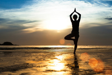 Wall Mural - Silhouette of a young woman practicing yoga on the beach.