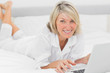 © WavebreakmediaMicro - Happy woman using her laptop on her bed smiling at camera