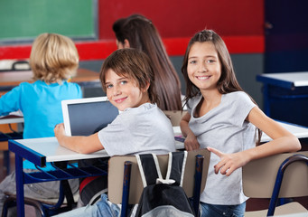 Schoolchildren With Digital Tablet Sitting In Classroom