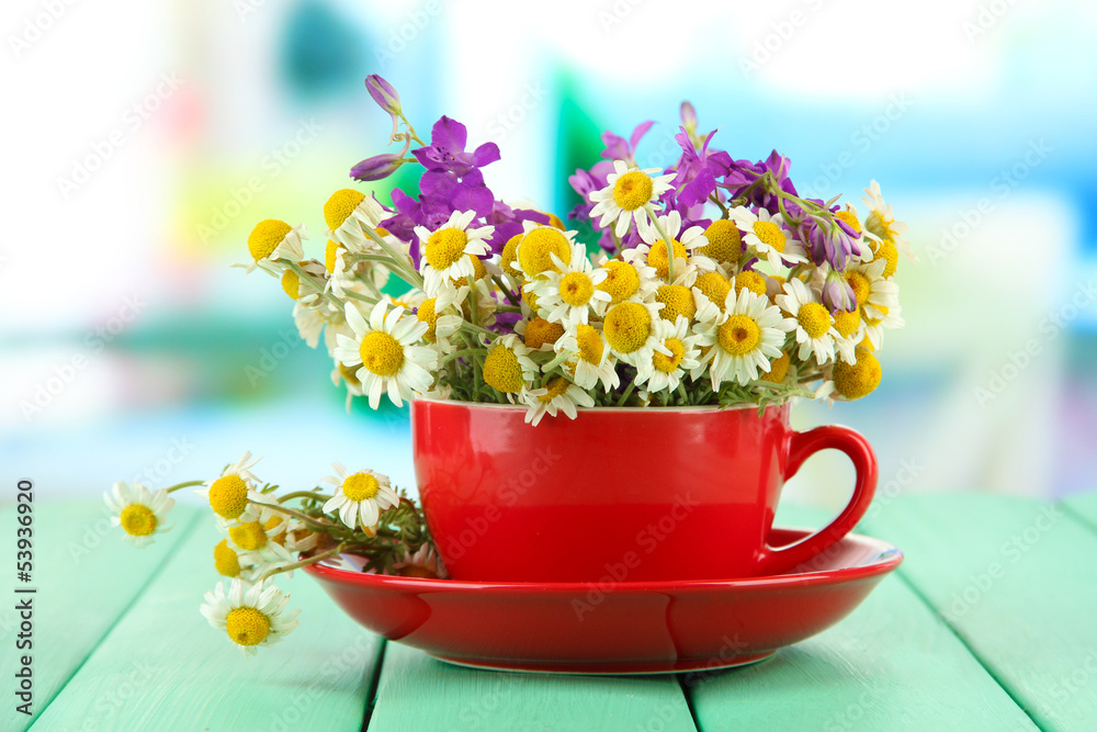 Bouquet of chamomile flowers in cup, on bright background