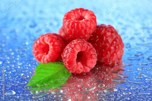 Fototapeta na wymiar Ripe sweet raspberries with drops, on blue background