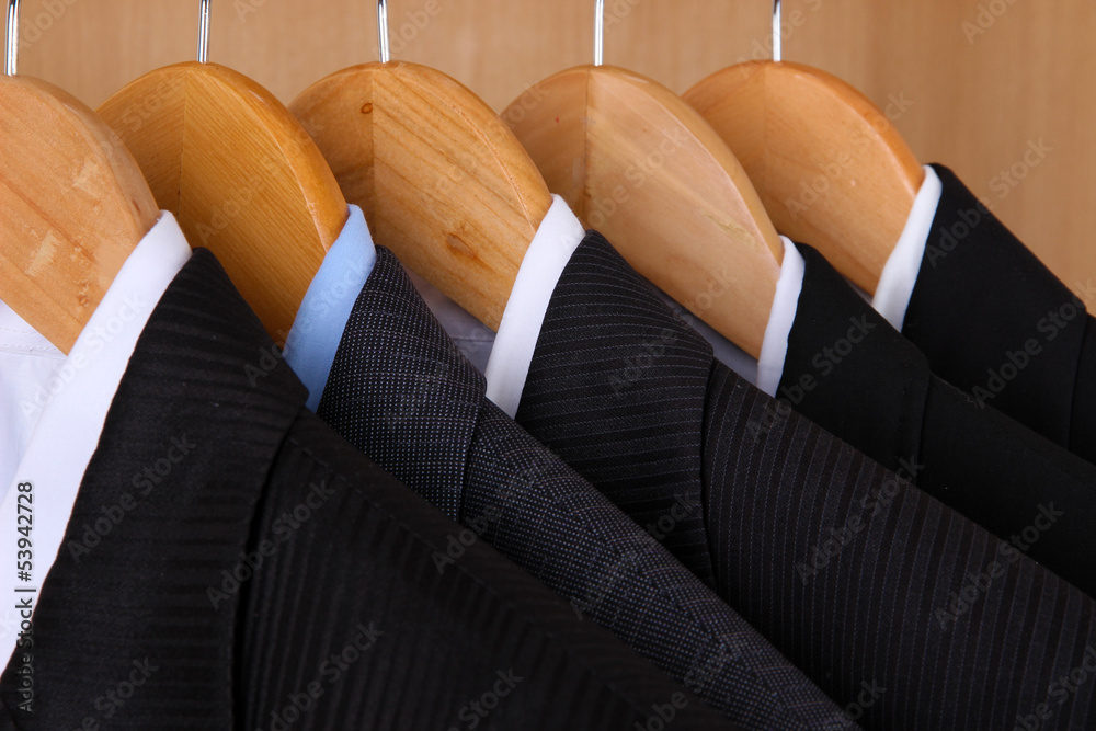 Suits with shirts on hangers on wooden background