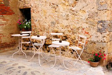 Fototapete - Cafe tables and chairs outside in a quaint corner of Tuscany