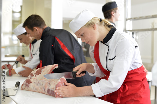 Fotografía Girl cutting meat during butcher training course