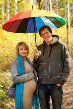 Pregnant Woman And A Man Walking Under Umbrella