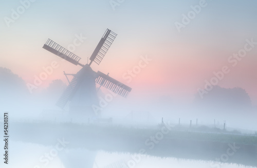 Fototapeta na wymiar windmill in dense fog at summer sunrise