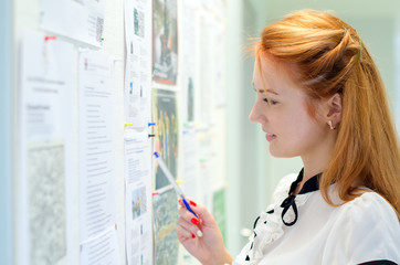 young female student looking through job offers on board