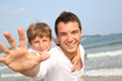 © goodluz - Man holding son on his back at the beach