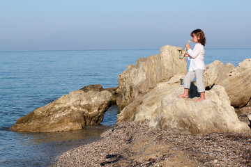 Wall Mural - little girl standing on a rock by the sea and playing saxophone