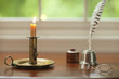 Colonial candle, quill pen and glasses on desk with window