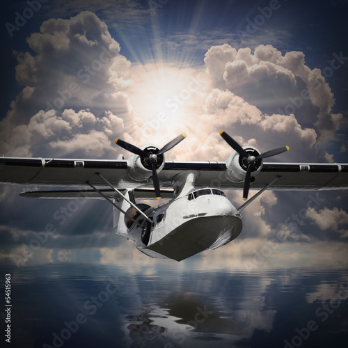 Fototapeta na wymiar Vintage seaplane flying against sunset over sea.