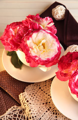 Roses in cups on napkins on wooden background