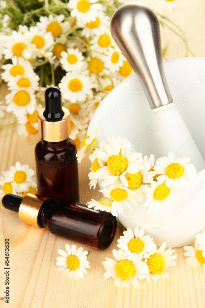 Essential oil and chamomile flowers in mortar on wooden table