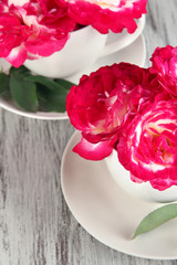 Roses in cups on wooden background