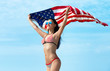 Smiling woman in bikini with American flag, blue sky