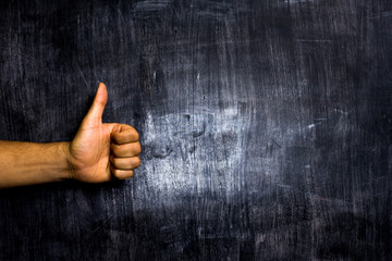 Hand giving thumbs up in front of blackboard