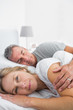 © WavebreakmediaMicro - Blonde woman smiling at camera as husband is sleeping