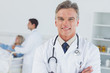 © WavebreakmediaMicro - Experienced doctor posing with doctor attending patient on backg