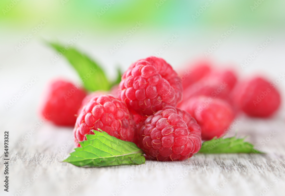 Ripe sweet raspberries on wooden table, on green background