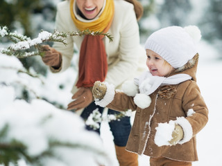 Wall Mural - Happy mother and baby playing with snow on branch