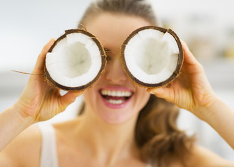 Smiling woman holding two pieces of coconut in front of eyes