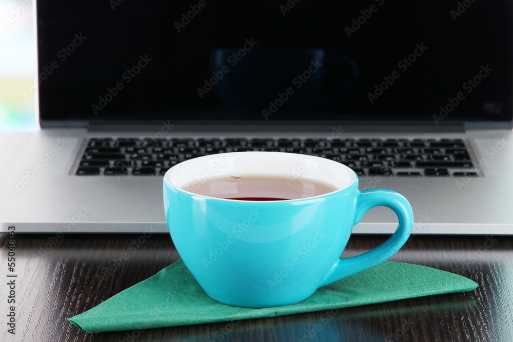 Blue cup on napkin on laptop background on wooden table