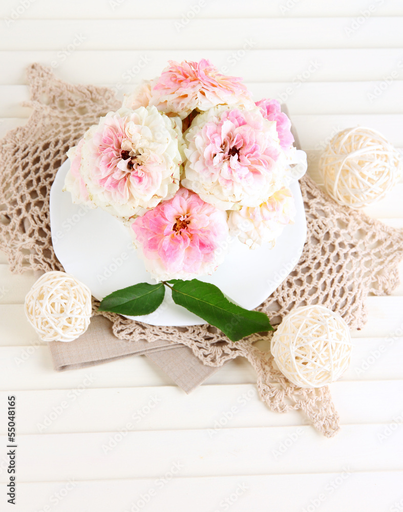 Roses in cup on napkins on wooden background