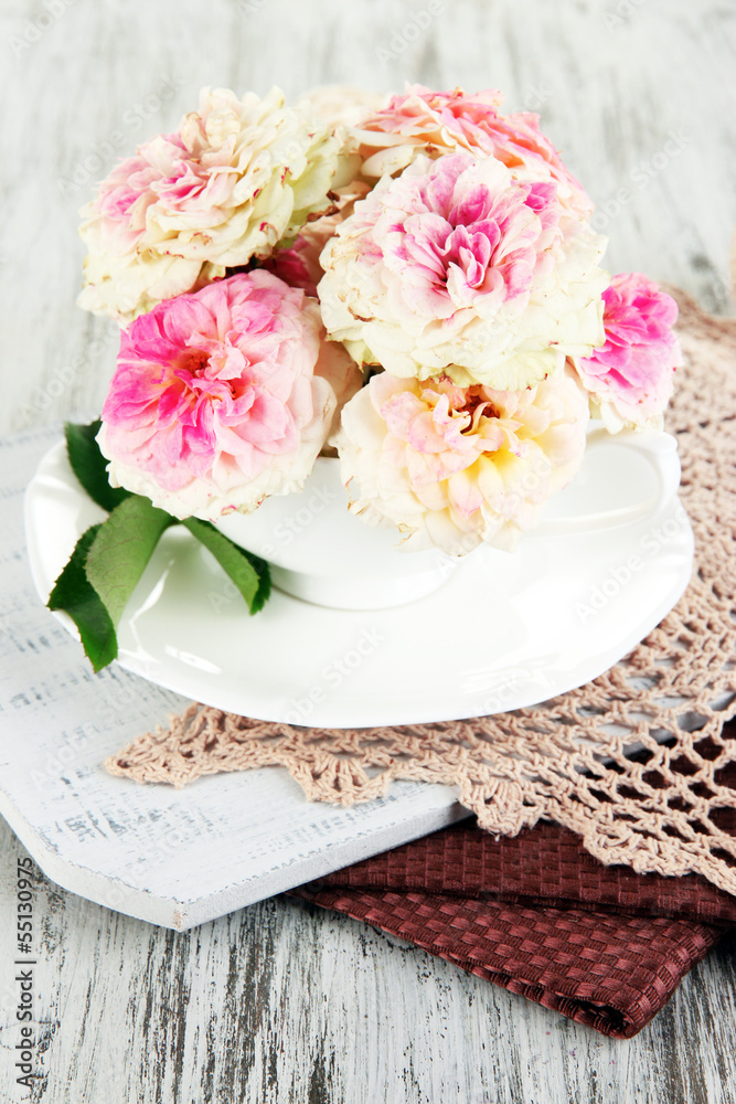 Roses in cup on napkins on  wooden background