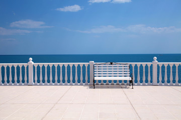 white bench, balustrade and empty terrace overlooking the sea