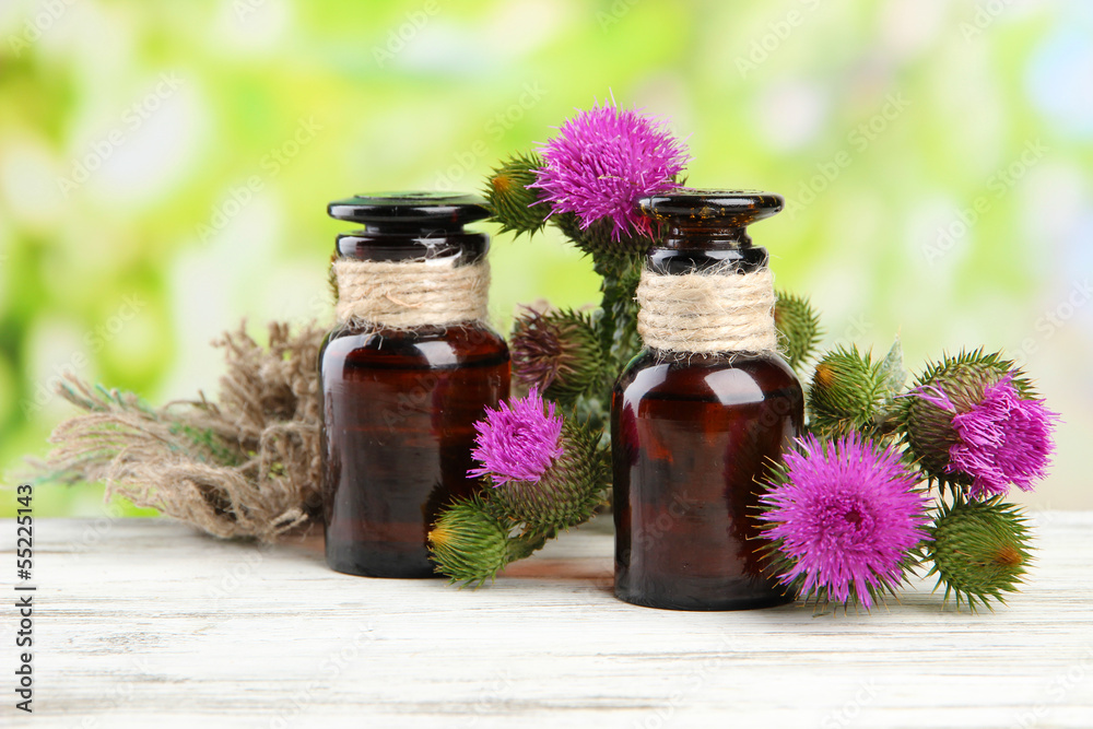 Medicine bottles with thistle flowers on nature background