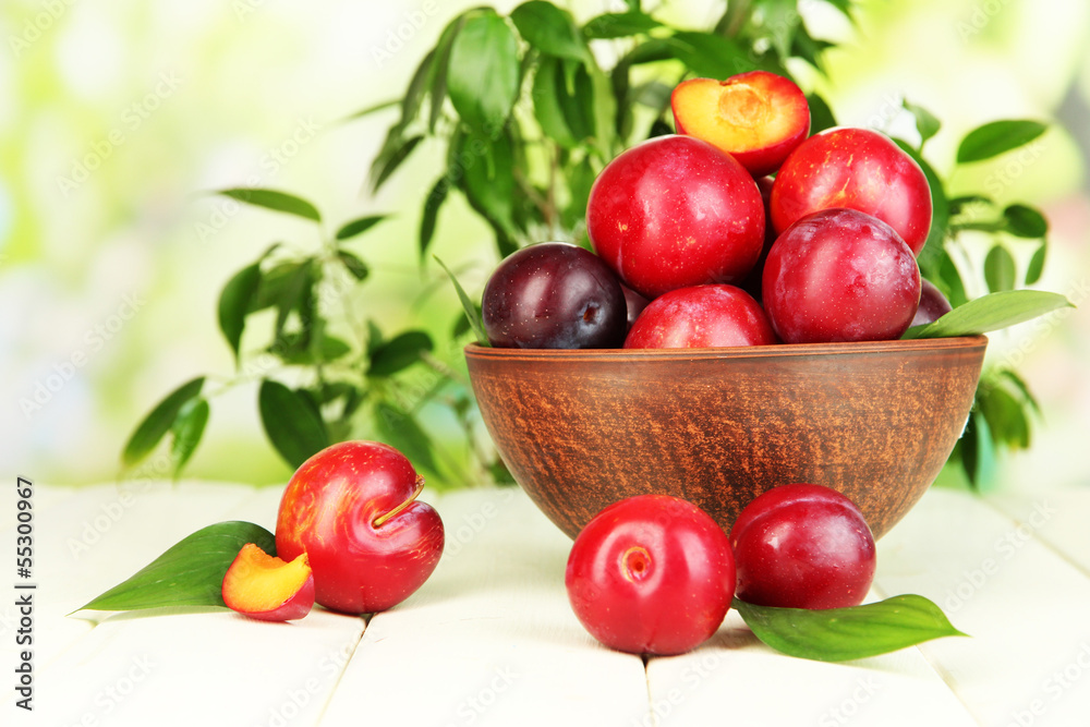 Ripe plums in bowl on wooden table on natural background