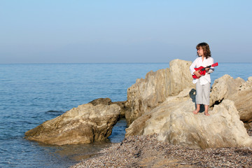 Wall Mural - little girl with guitar standing on a rock