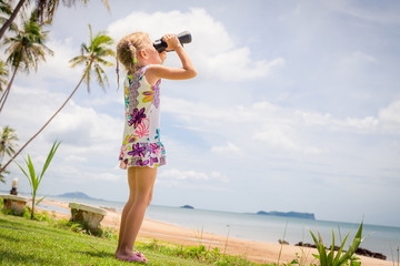 little girl on the beach looking at the sky through binoculars