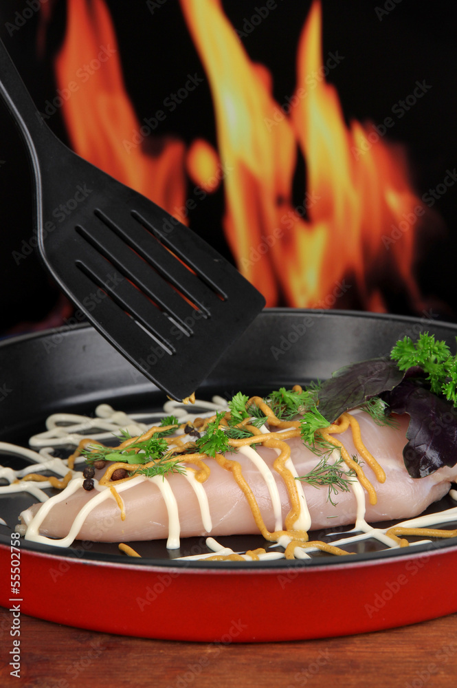 Raw chicken fillets on dripping pan, on fire background