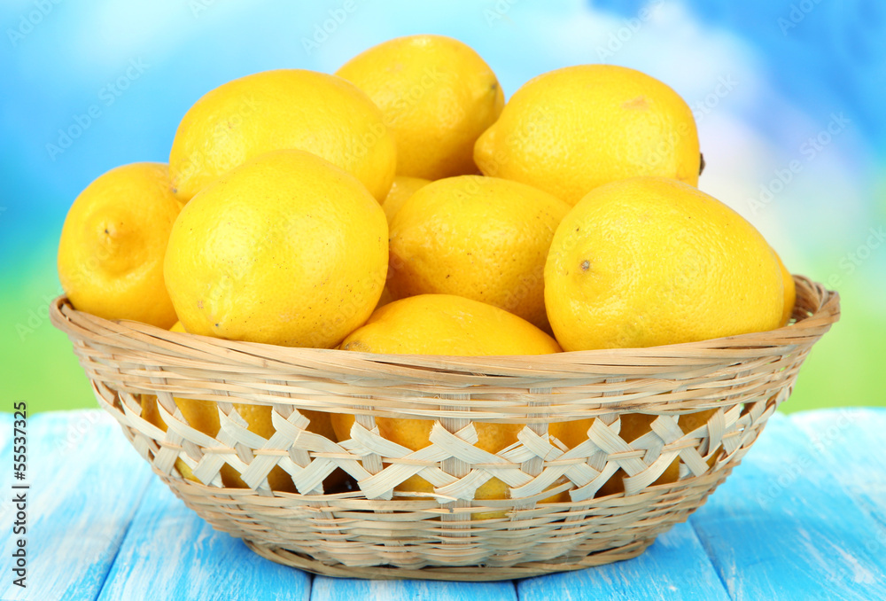 Ripe lemons in wicker basket on table on bright background