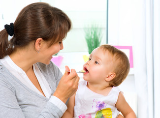 Fototapete - Mother Feeding Her Baby Girl with a Spoon