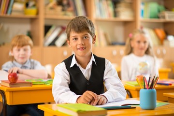 Fototapete - Little schoolboy  sitting behind school desk