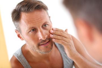 Man in bathroom applying cosmetics on his face