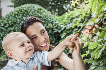 smiling mother and son pointing and looking at a butterfly in the garden